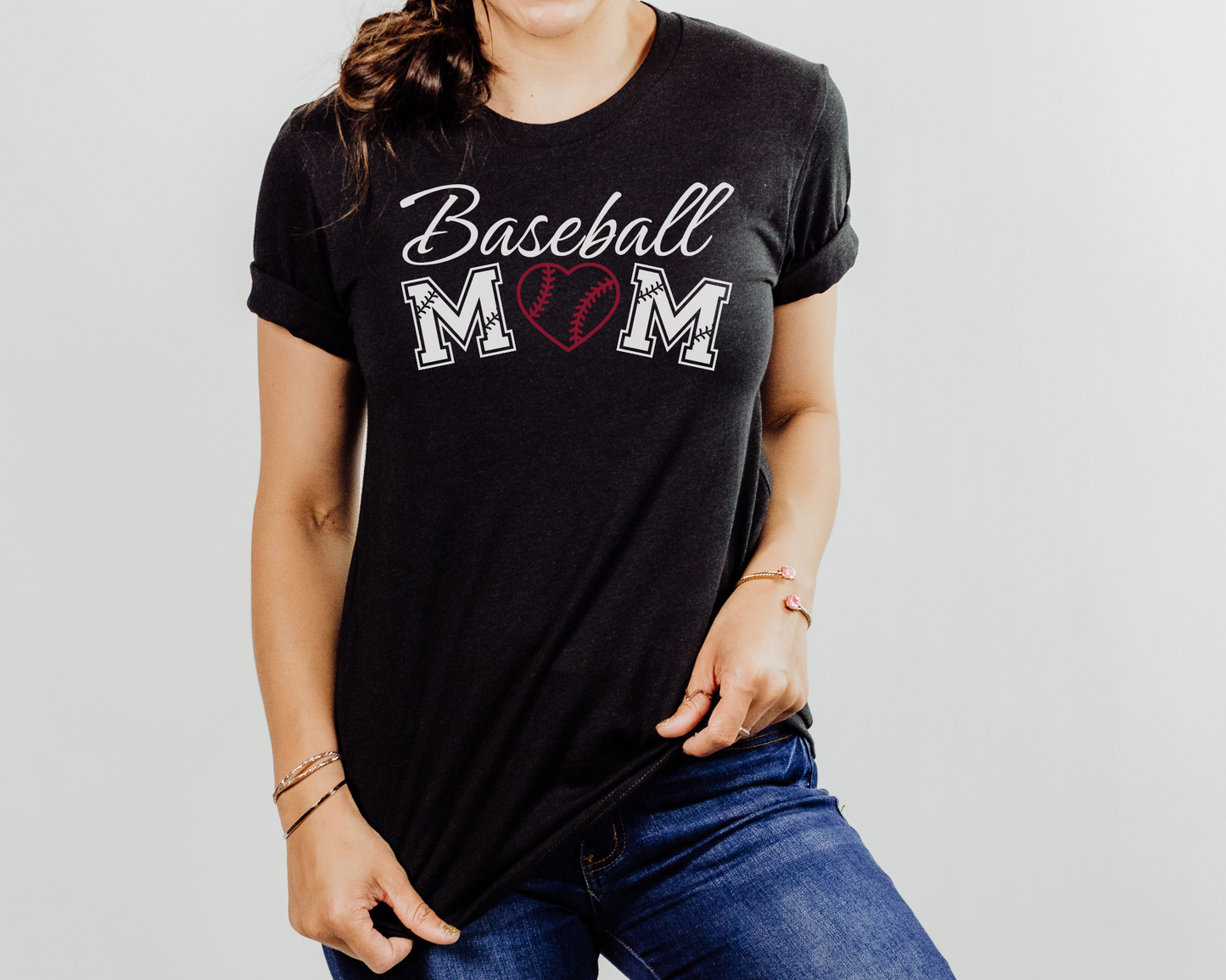 A model wearing a black t-shirt with a 'Baseball Mom' design. The design features white cursive font for "baseball" and white baseball font for "mom". A red baseball heart replaces the "O" in "mom".