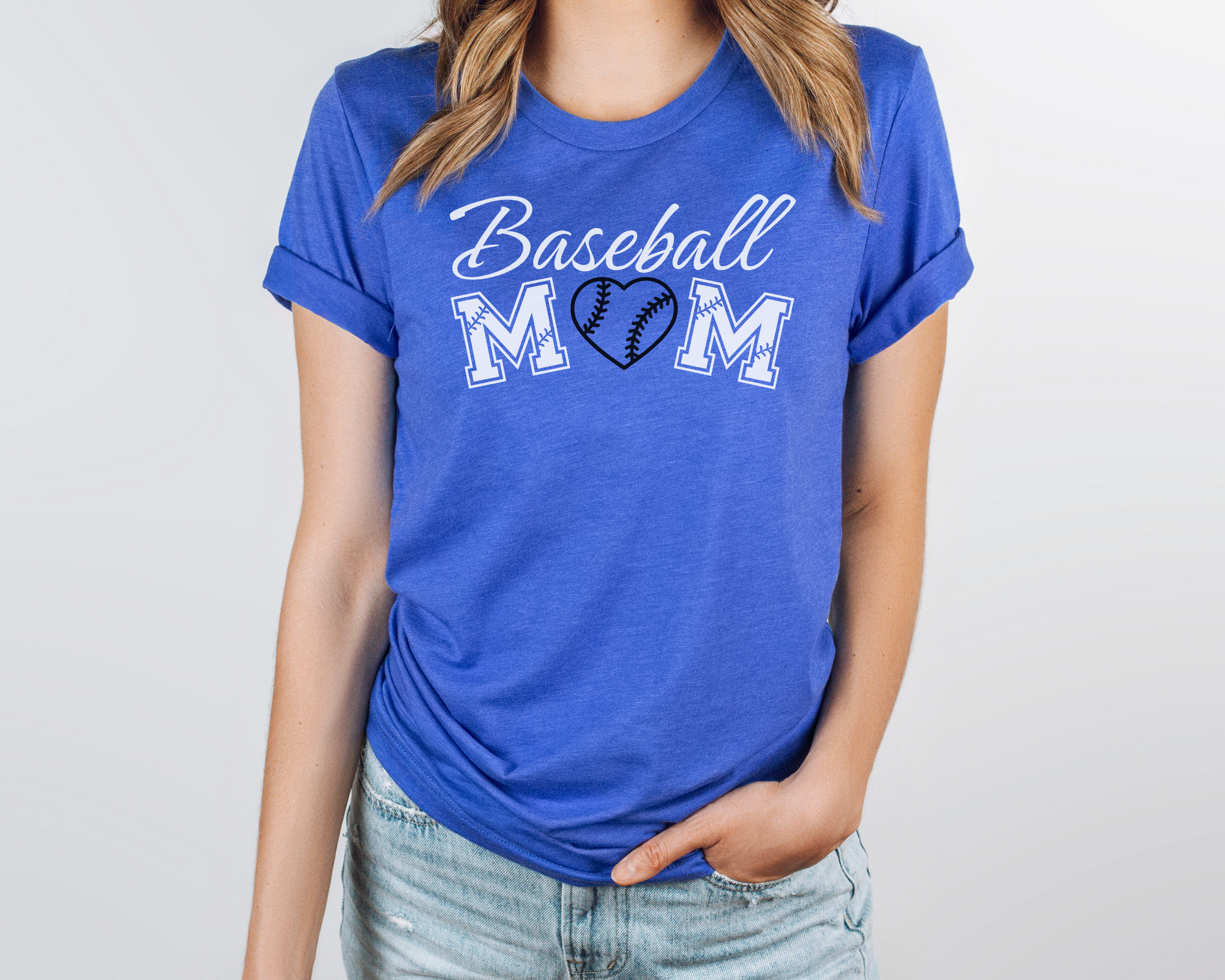 A model wearing a blue t-shirt with a 'Baseball Mom' design. The design features white cursive font for "baseball" and white baseball font for "mom". A black baseball heart replaces the "O" in "mom".