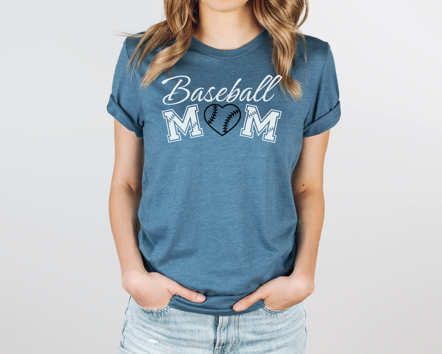 A model wearing a deep teal t-shirt with a 'Baseball Mom' design. The design features white cursive font for "baseball" and white baseball font for "mom". A black baseball heart replaces the "O" in "mom".