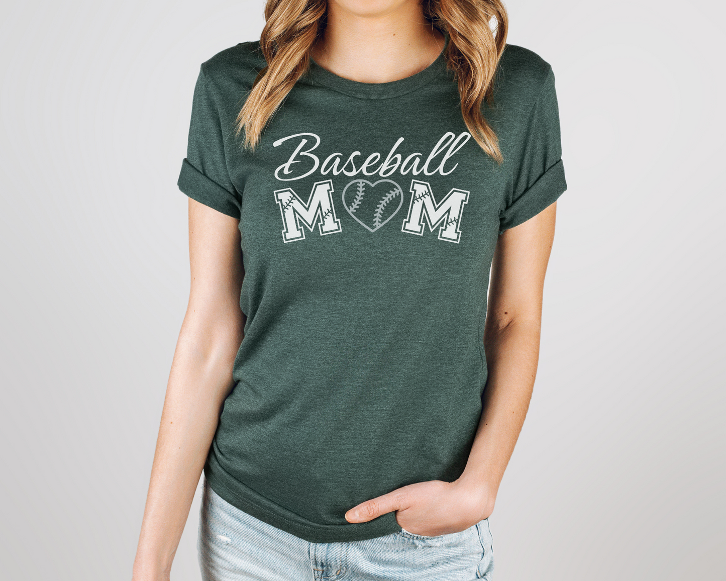 A model wearing a green t-shirt with a 'Baseball Mom' design. The design features white cursive font for "baseball" and white baseball font for "mom". A silver baseball heart replaces the "O" in "mom".