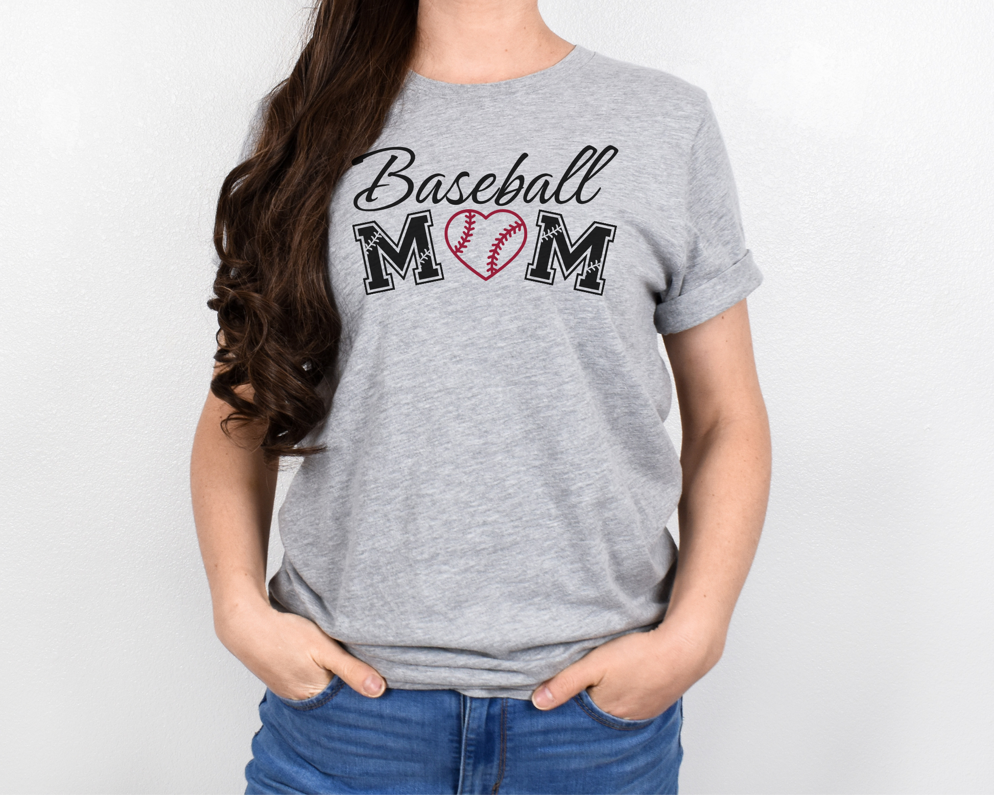 A model wearing a light gray t-shirt with a 'Baseball Mom' design. The design features black cursive font for "baseball" and black baseball font for "mom". A red baseball heart replaces the "O" in "mom".