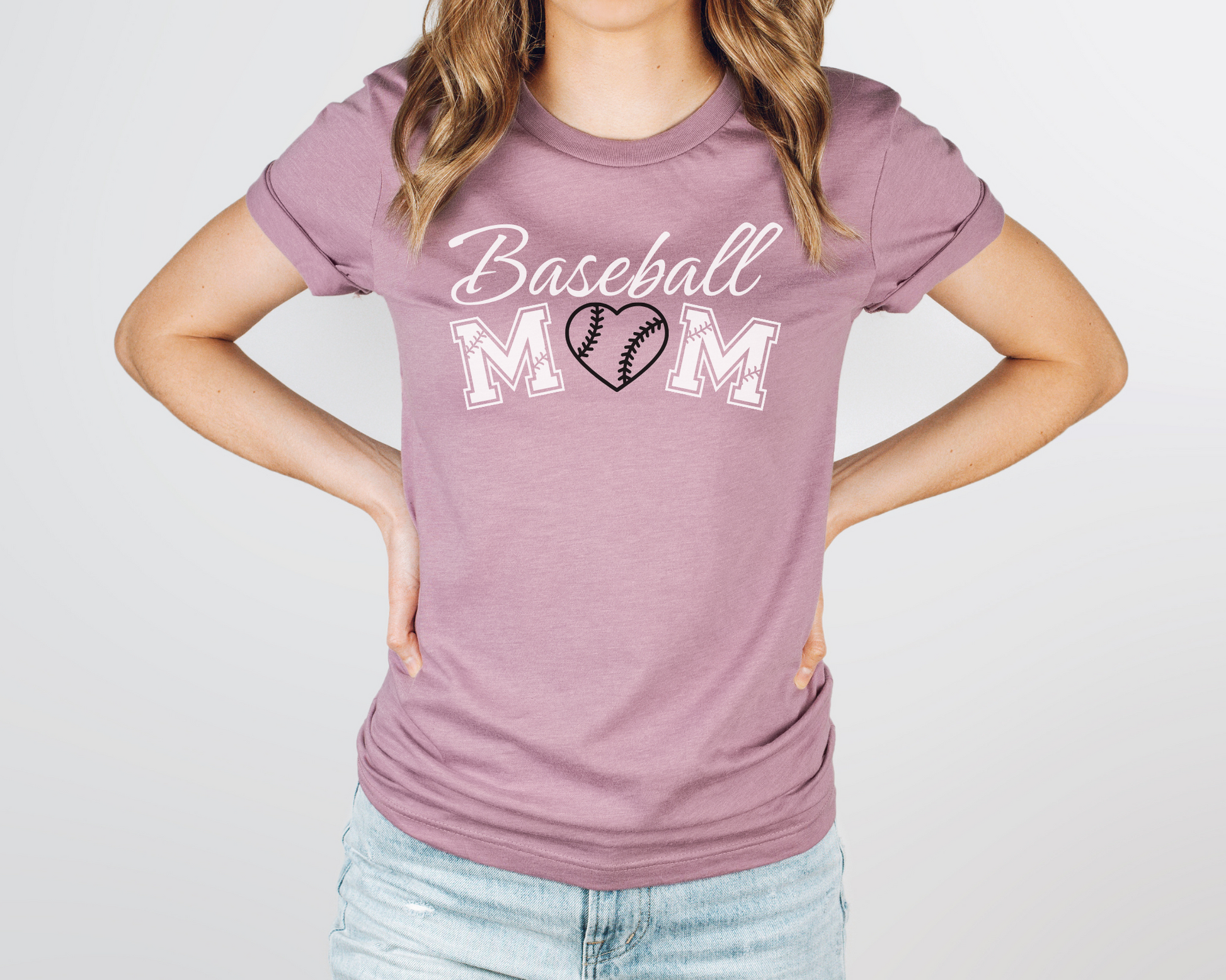 A model wearing a pink t-shirt with a 'Baseball Mom' design. The design features white cursive font for "baseball" and white baseball font for "mom". A black baseball heart replaces the "O" in "mom".