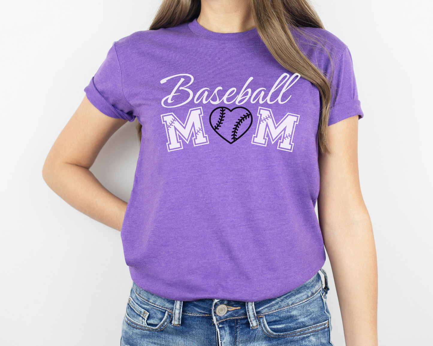 A model wearing a purple t-shirt with a 'Baseball Mom' design. The design features white cursive font for "baseball" and white baseball font for "mom". A black baseball heart replaces the "O" in "mom".