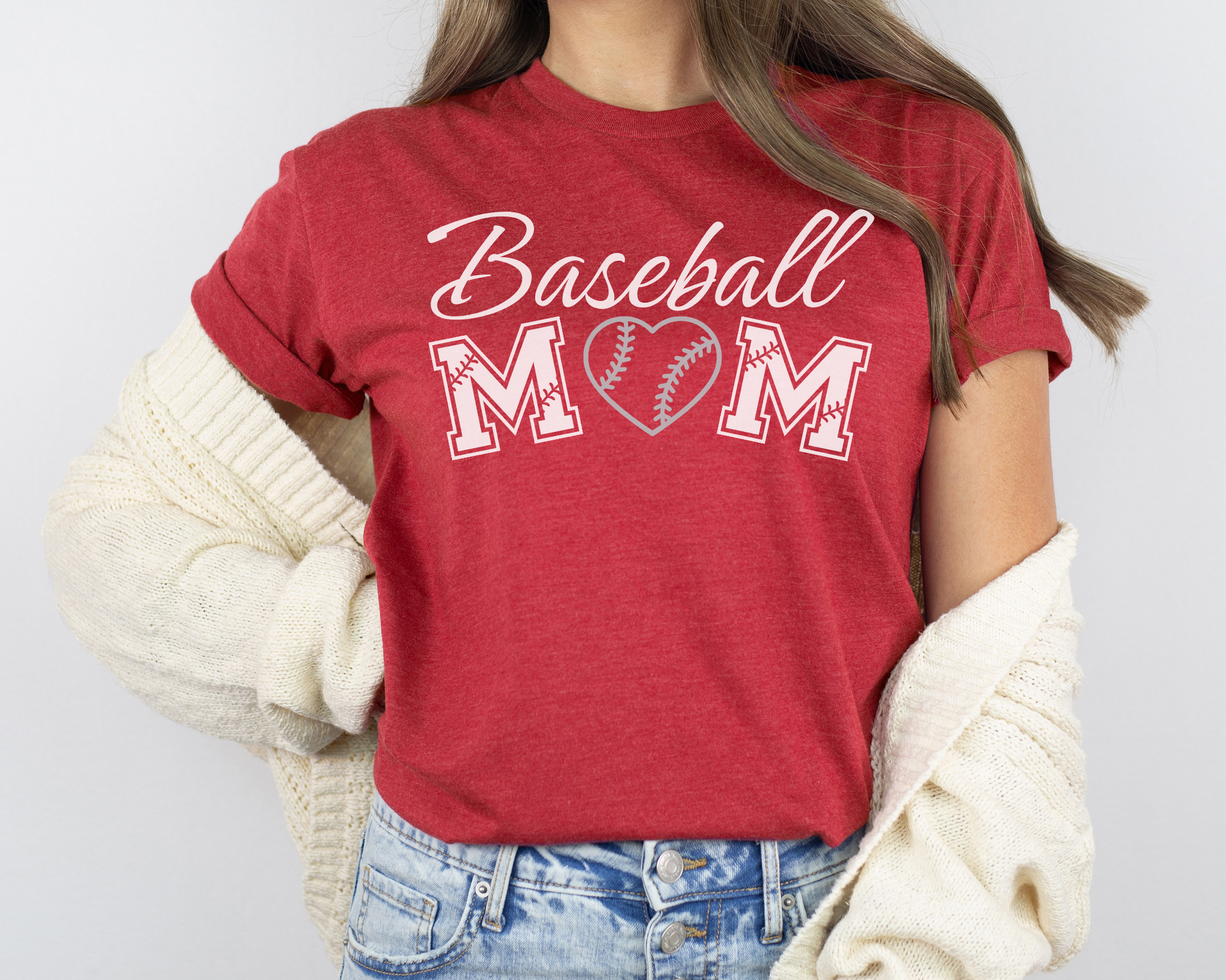 A model wearing a red t-shirt with a 'Baseball Mom' design. The design features white cursive font for "baseball" and white baseball font for "mom". A silver baseball heart replaces the "O" in "mom".